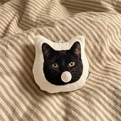 Black cat Chew Chew Club custom plush keychain with bubble detail resting on striped beige bedding